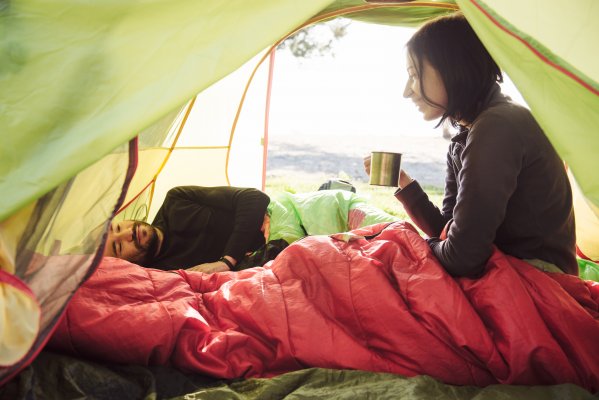 girl in red sleeping bag in green tent holding mug sleeping bags
